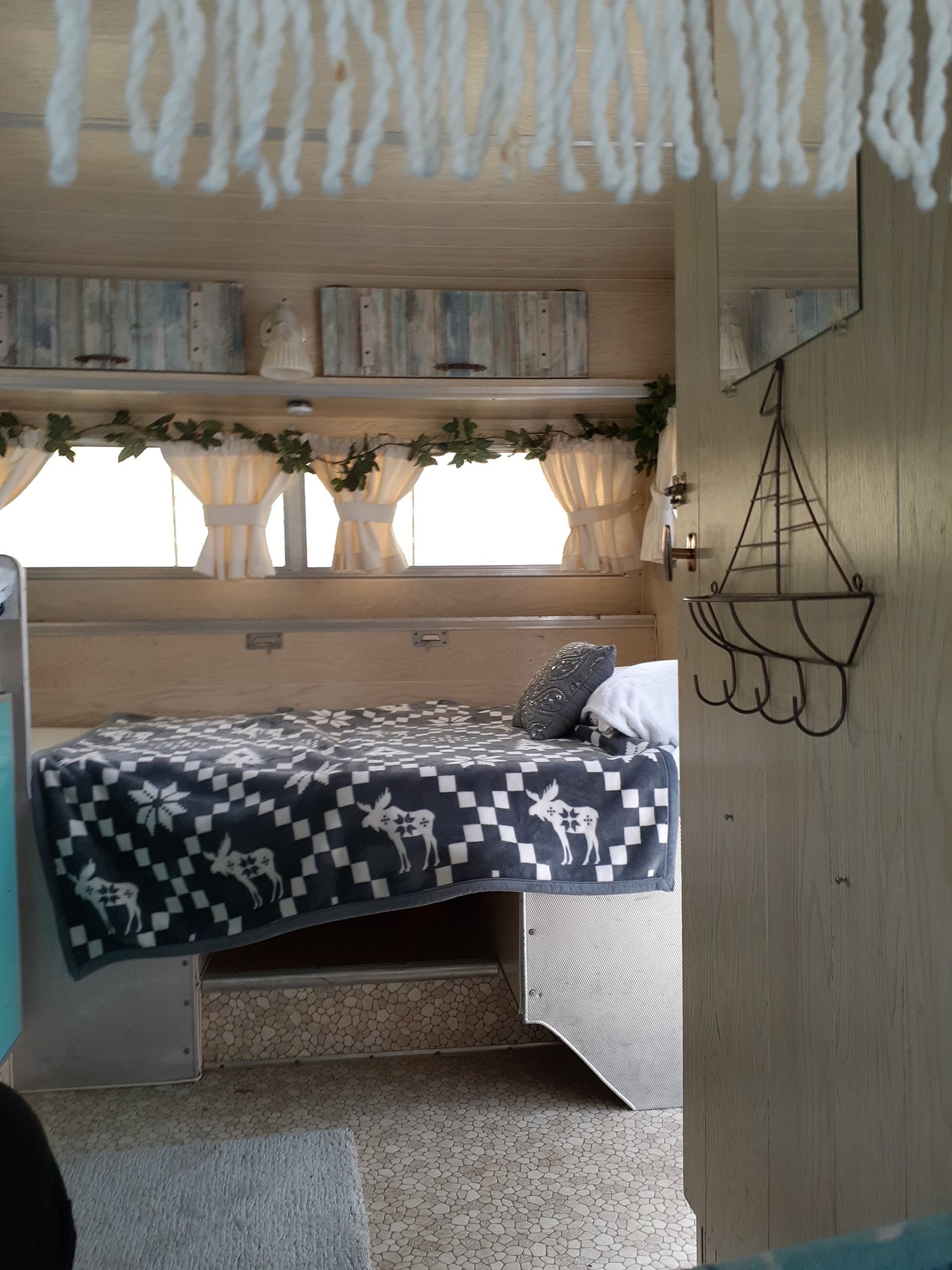 Cozy RV rental bedroom interior with a patterned blanket, rustic decor, and bright windows.