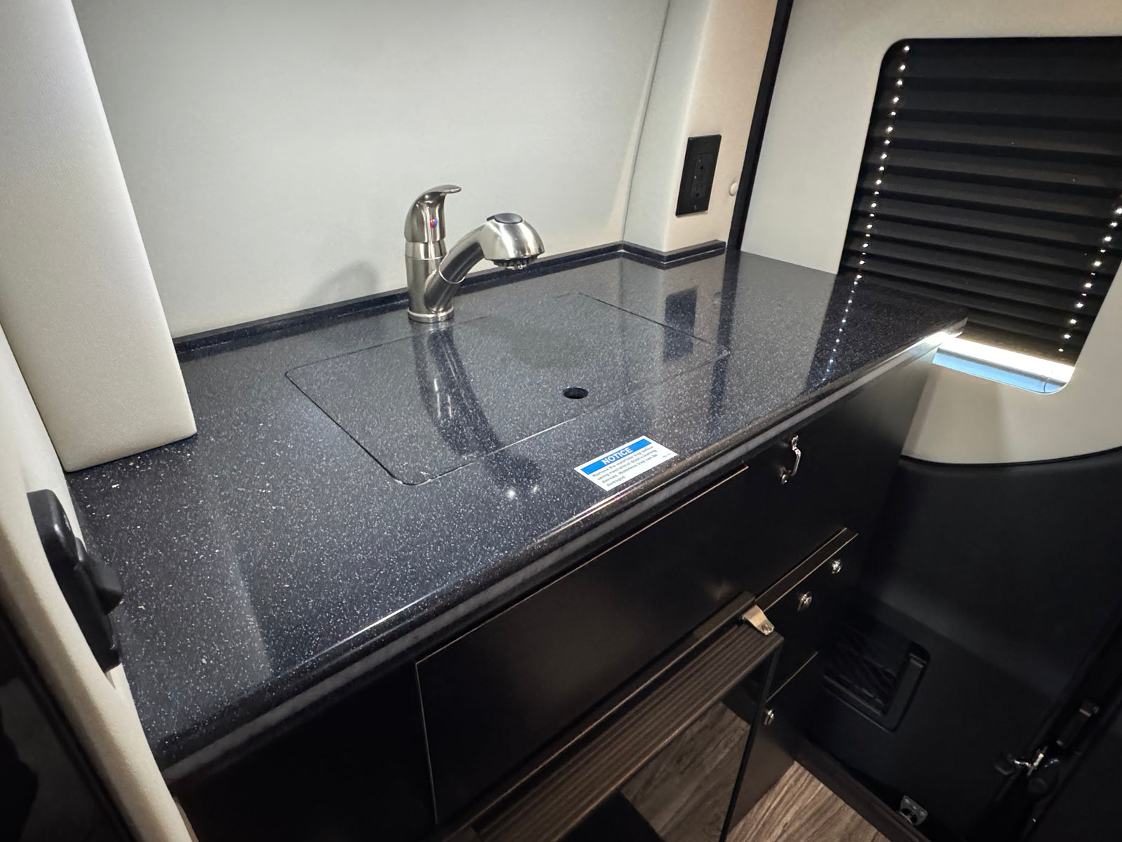 This RV rental features a compact kitchenette with a pull-out faucet, dark countertop, and integrated sink for efficient travel.