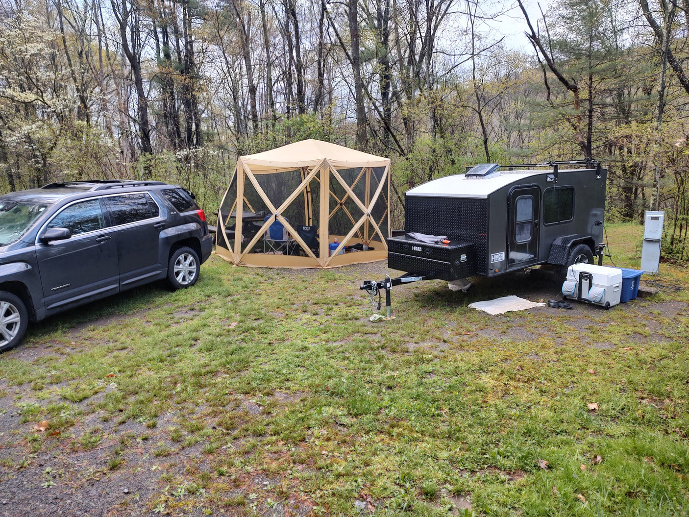 Wooded campsite featuring an SUV, screen tent, and teardrop RV trailer, ready for your RV rental getaway.