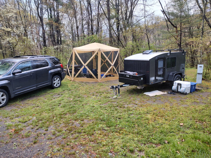 Wooded campsite featuring an SUV, screen tent, and teardrop RV trailer, ready for your RV rental getaway.
