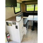RV rental interior: cozy dinette with bench seating, table, and kitchen counter with TV. Ready for your adventure! — photo 10