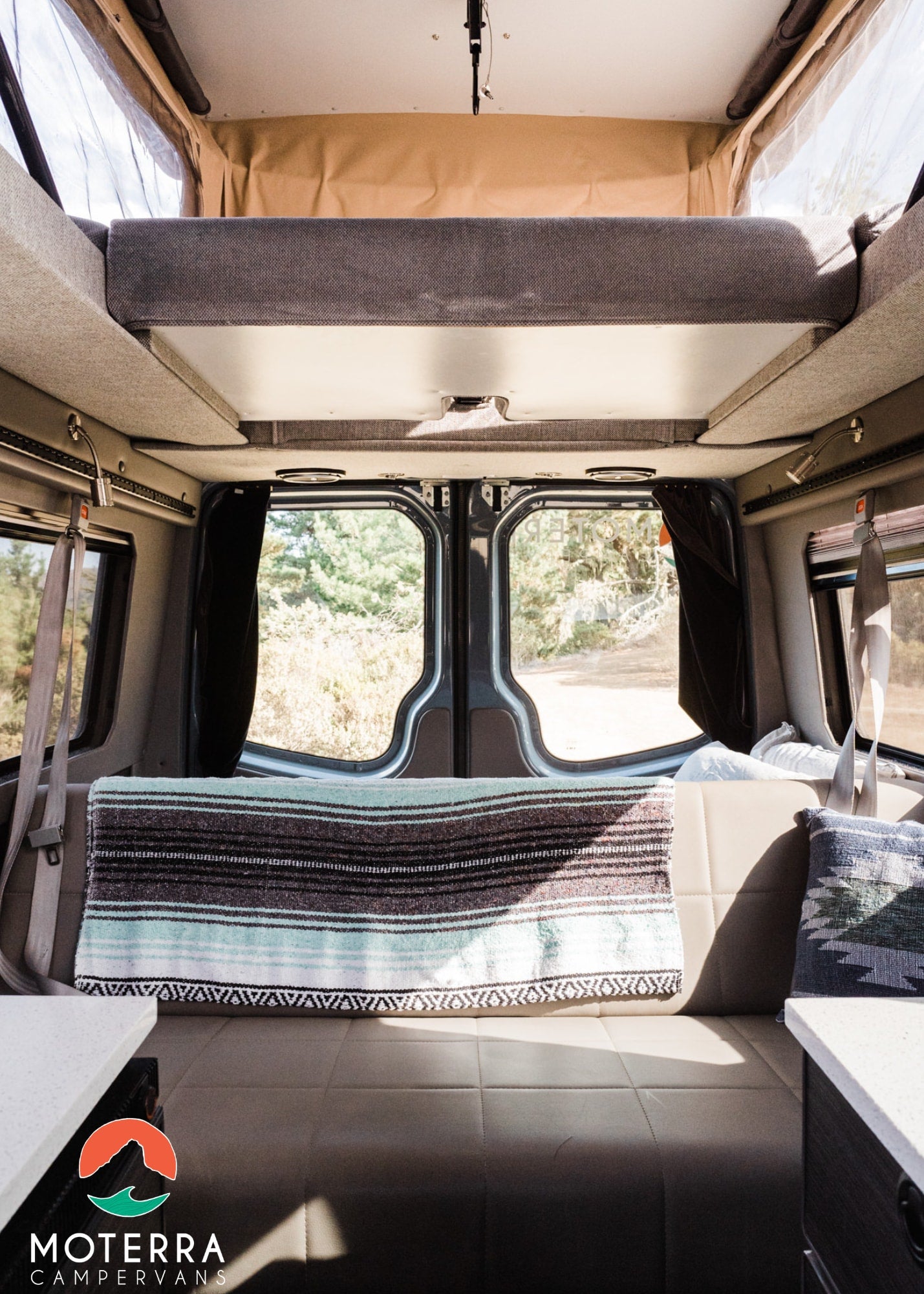 and a comfortable bed.|Cozy pop-top campervan bed ready for your RV rental adventure. Bright interior with scenic window views.|RV rental interior: Built-in fridge