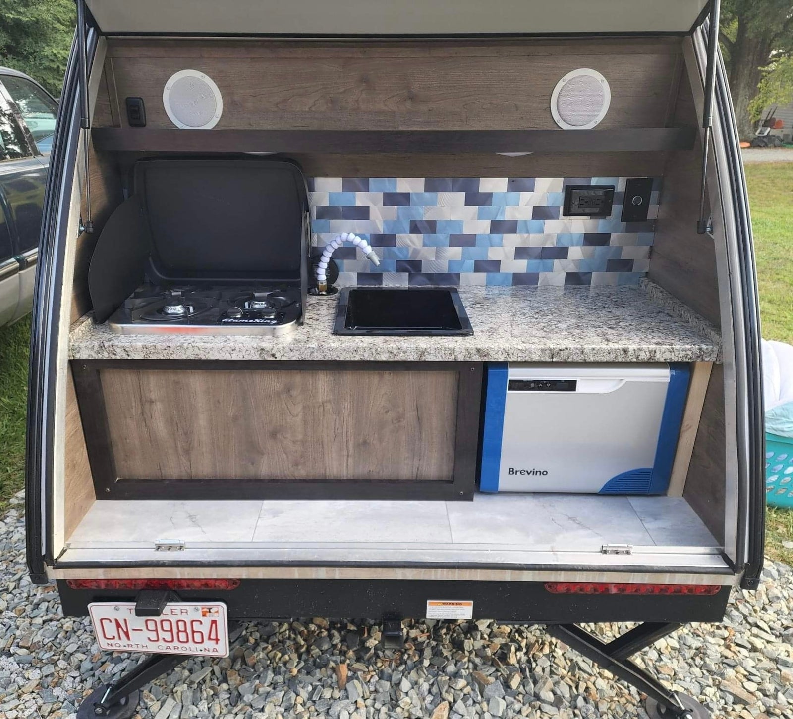 View this RV rental's detailed outdoor kitchen: stove, sink, Brevino cooler, and patterned backsplash. Ideal for camping.