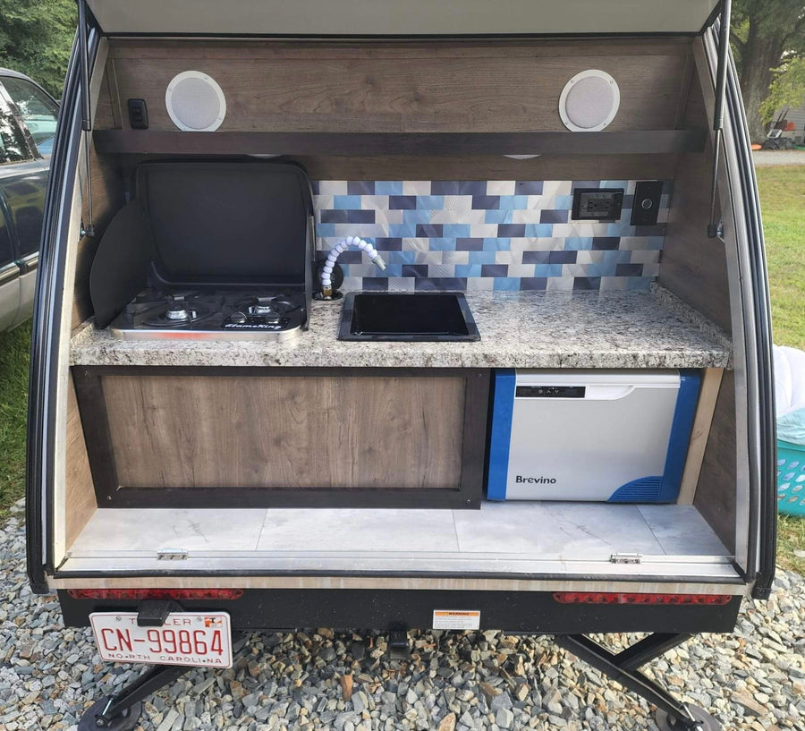 View this RV rental's detailed outdoor kitchen: stove, sink, Brevino cooler, and patterned backsplash. Ideal for camping.