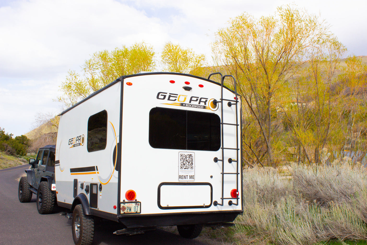 A white Geo Pro RV rental, towed by a Jeep, parked on a road. Ready for scenic road trips and outdoor adventures.
