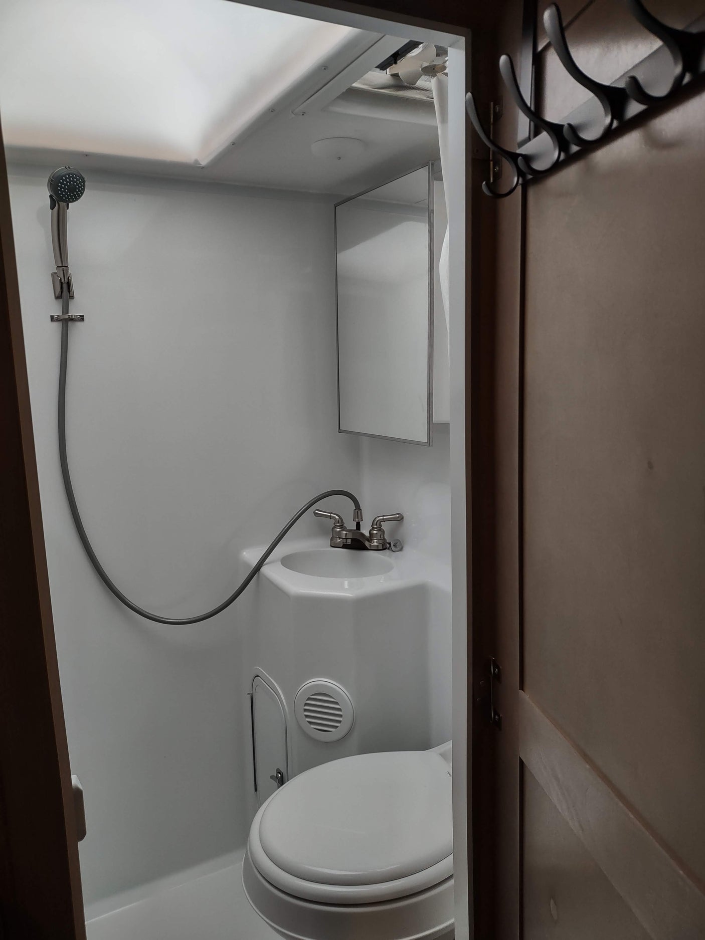 RV rental bathroom: A compact space with white fixtures including a toilet, sink with shower hose, and mirror. Overhead storage visible.