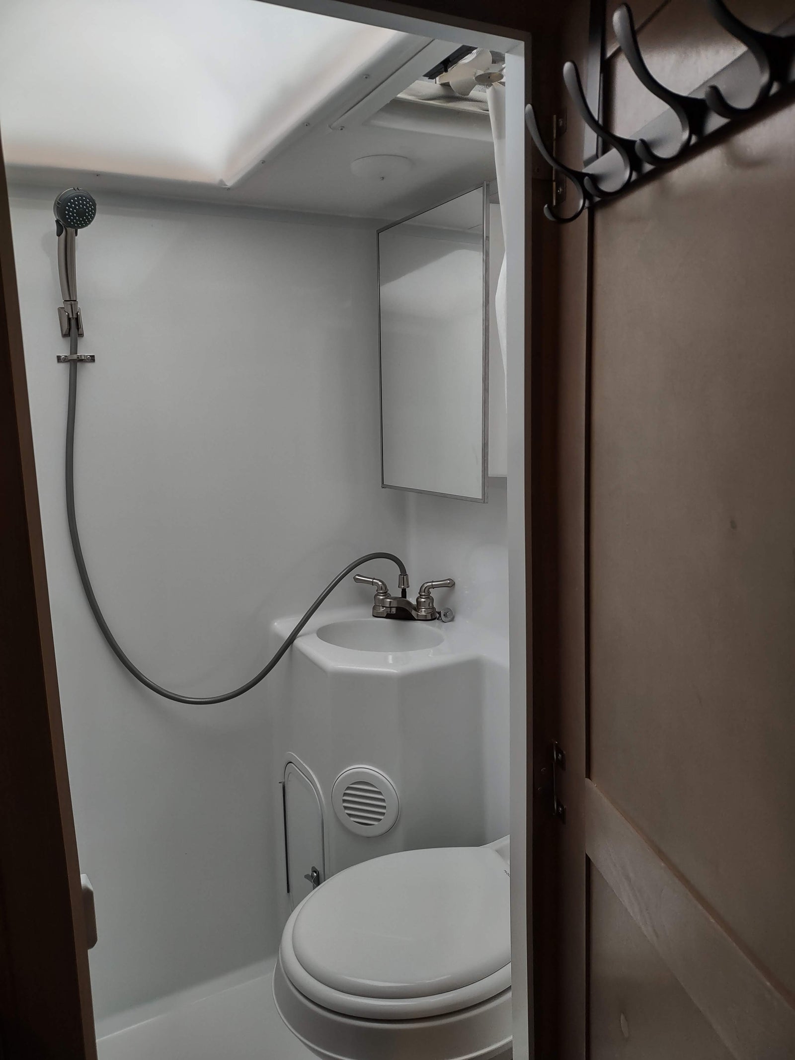 RV rental bathroom: A compact space with white fixtures including a toilet, sink with shower hose, and mirror. Overhead storage visible.