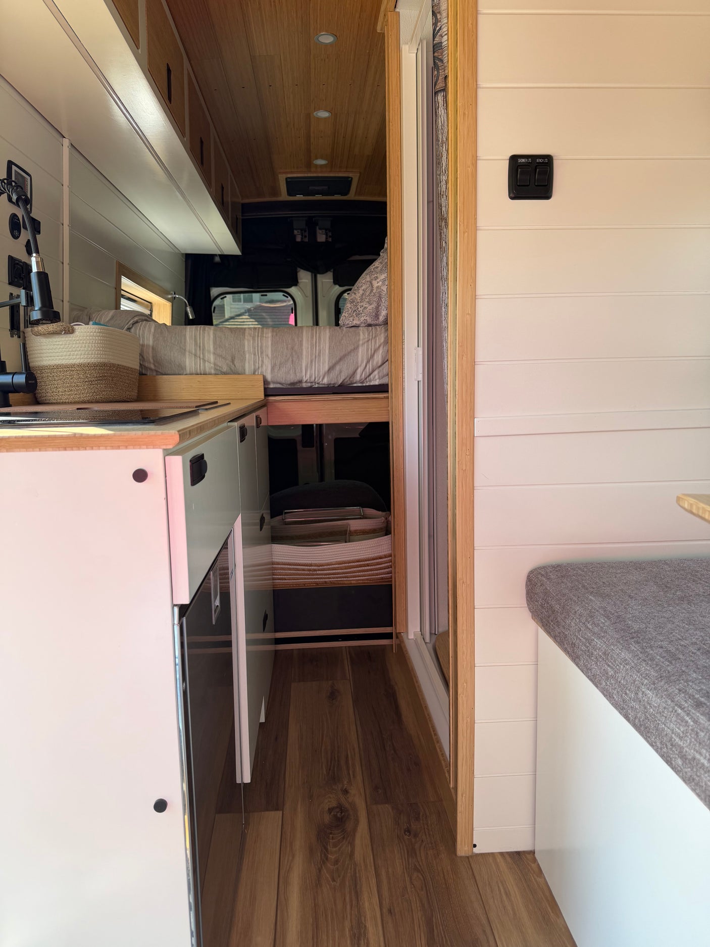 This RV rental's interior features a compact kitchen, raised bed, and seating area with modern wood and white finishes.