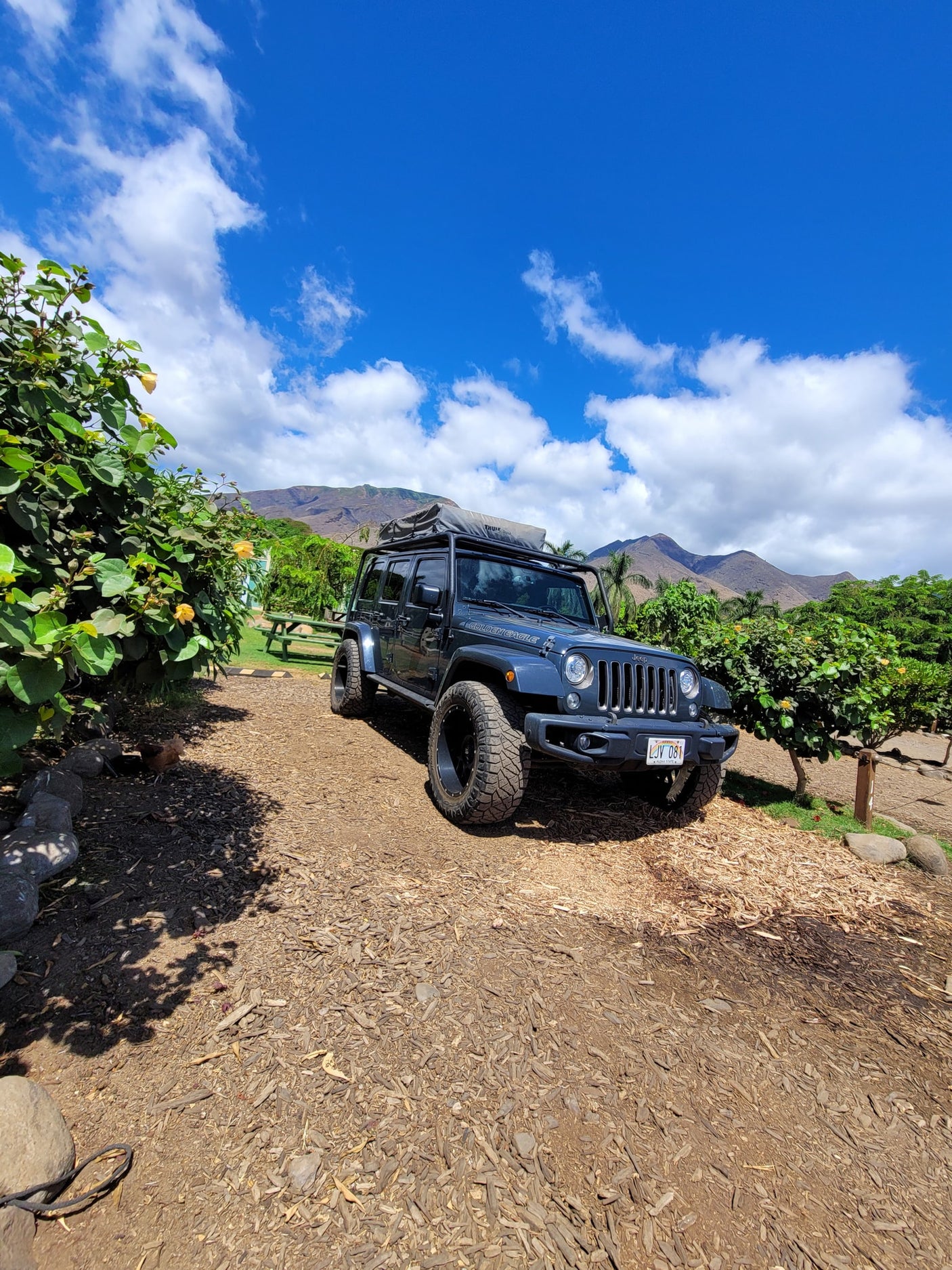 Adventure-ready Jeep Wrangler RV rental with rooftop tent against Hawaiian mountains & blue sky. Perfect for outdoor travel!