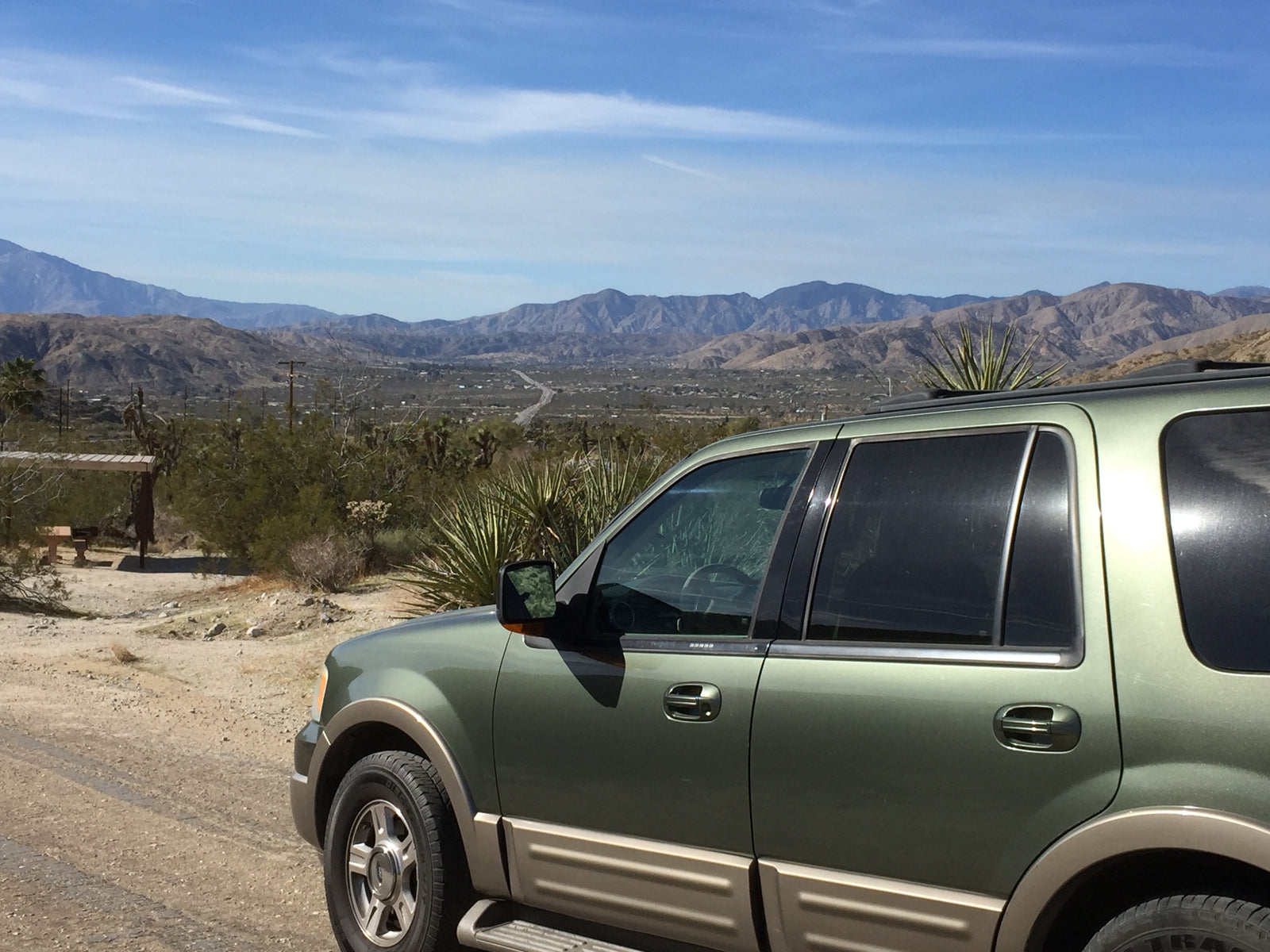 Green SUV parked on a dirt road, offering scenic desert views and distant mountains. Perfect for an RV rental adventure.