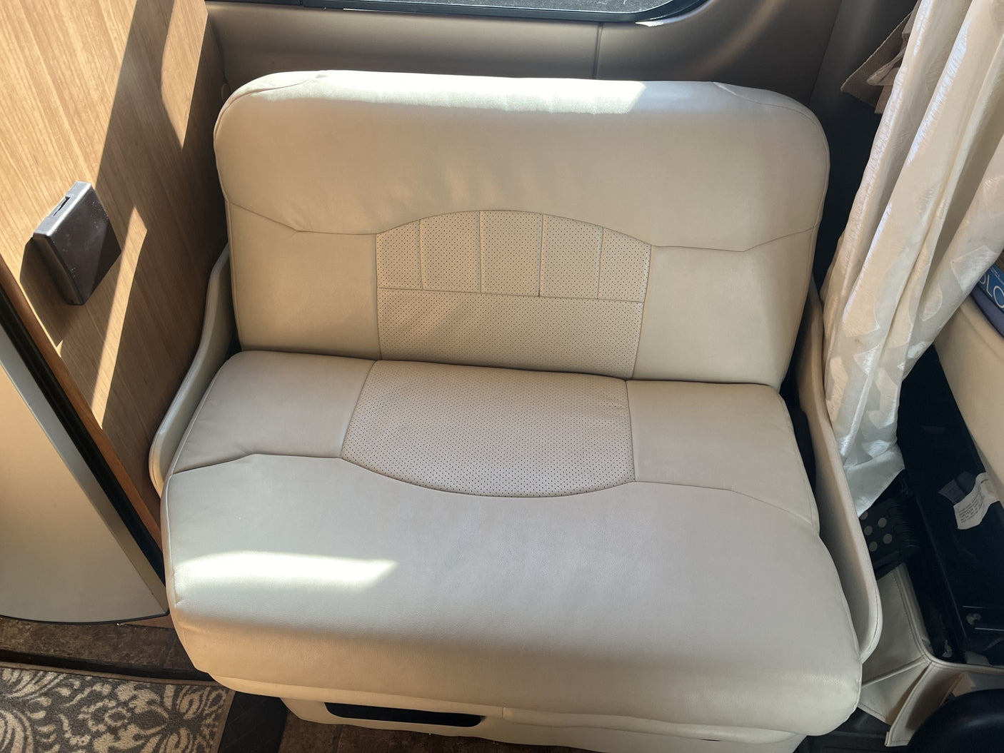 A cream leather RV rental bench seat, with perforated sections, inside a motorhome for comfortable travel.