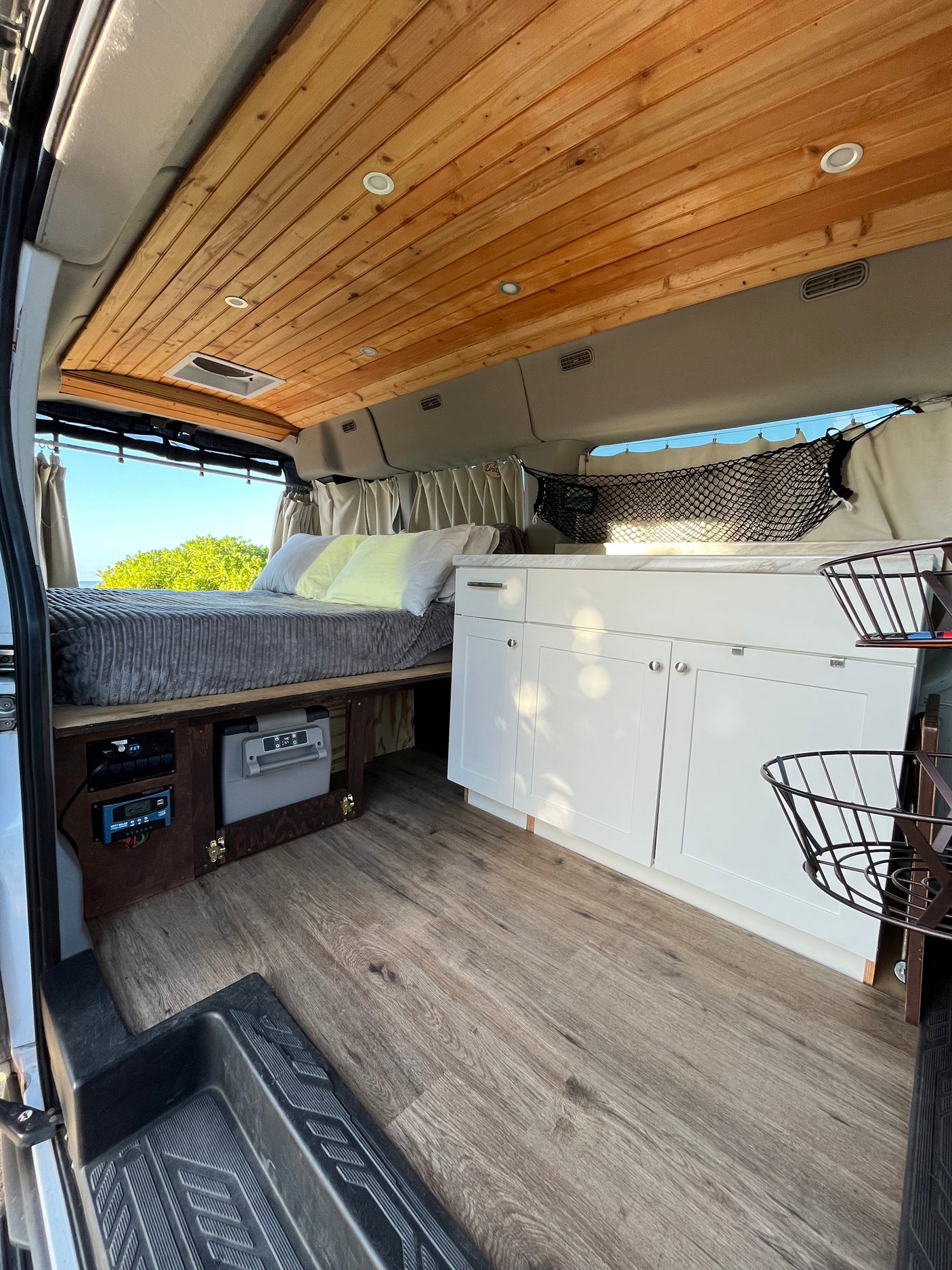 Modern RV rental interior featuring a comfy bed, kitchen, wood ceiling, and scenic window views.