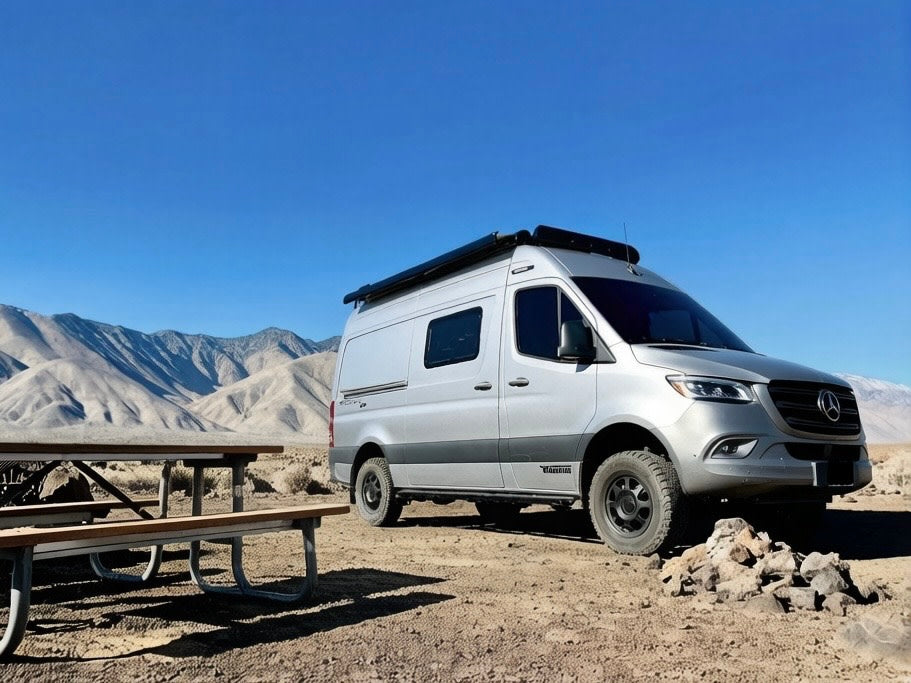 Silver Mercedes Sprinter RV rental in a desert mountain landscape, with a picnic table nearby for outdoor adventures.