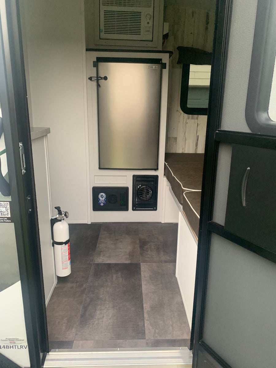 Compact RV rental interior with refrigerator, AC, and a fire extinguisher. Ideal for comfortable travel.
