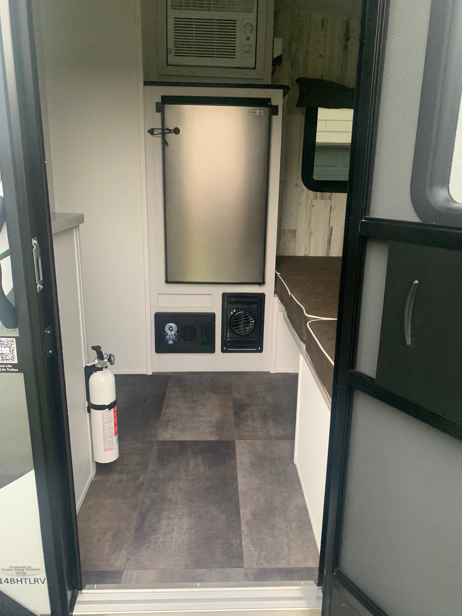 Compact RV rental interior with refrigerator, AC, and a fire extinguisher. Ideal for comfortable travel.