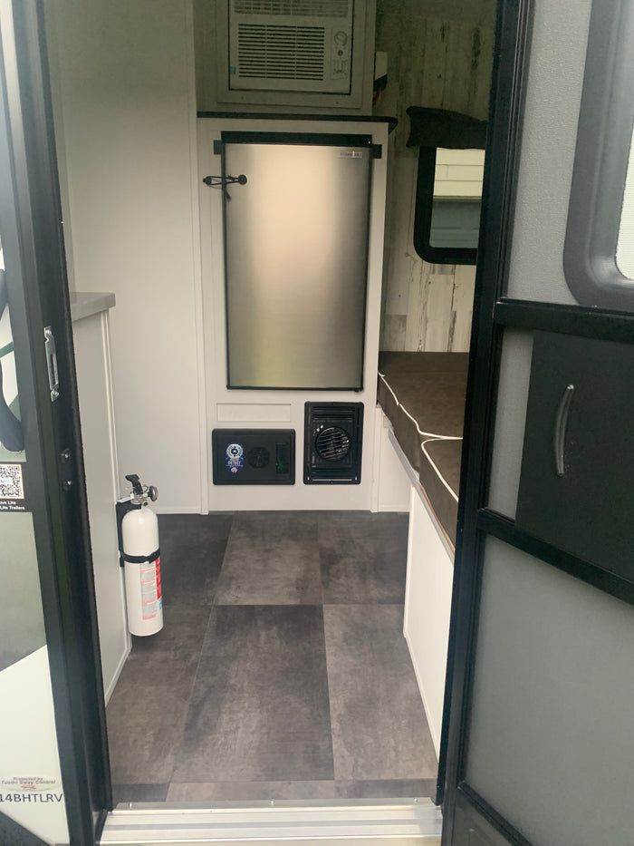 Compact RV rental interior with refrigerator, AC, and a fire extinguisher. Ideal for comfortable travel.