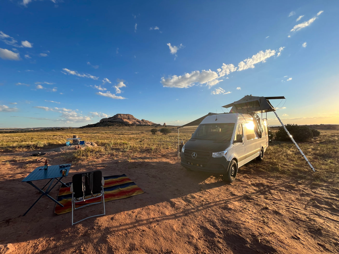 RV rental van with rooftop tent, set up for camping in a scenic desert landscape with mountains.