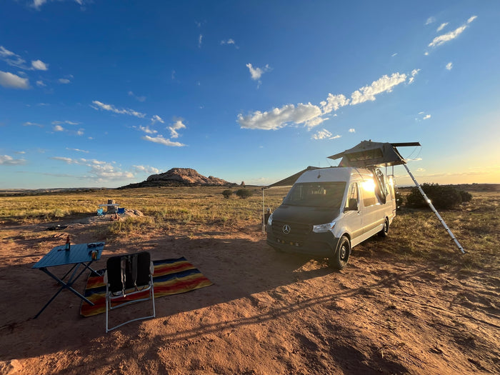 RV rental van with rooftop tent, set up for camping in a scenic desert landscape with mountains.