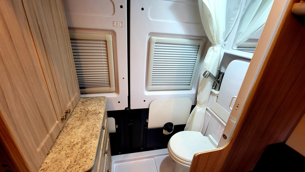 Compact RV rental: a bathroom with toilet and shower, plus a counter/cabinetry. Windows and 'EXIT' sign visible. — photo 8