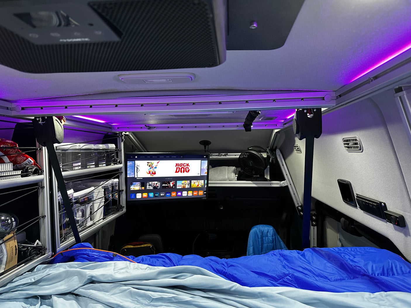 Inside a modern rv rental: a cozy bed, Vizio TV for entertainment, organized overhead storage, and ambient purple lighting.