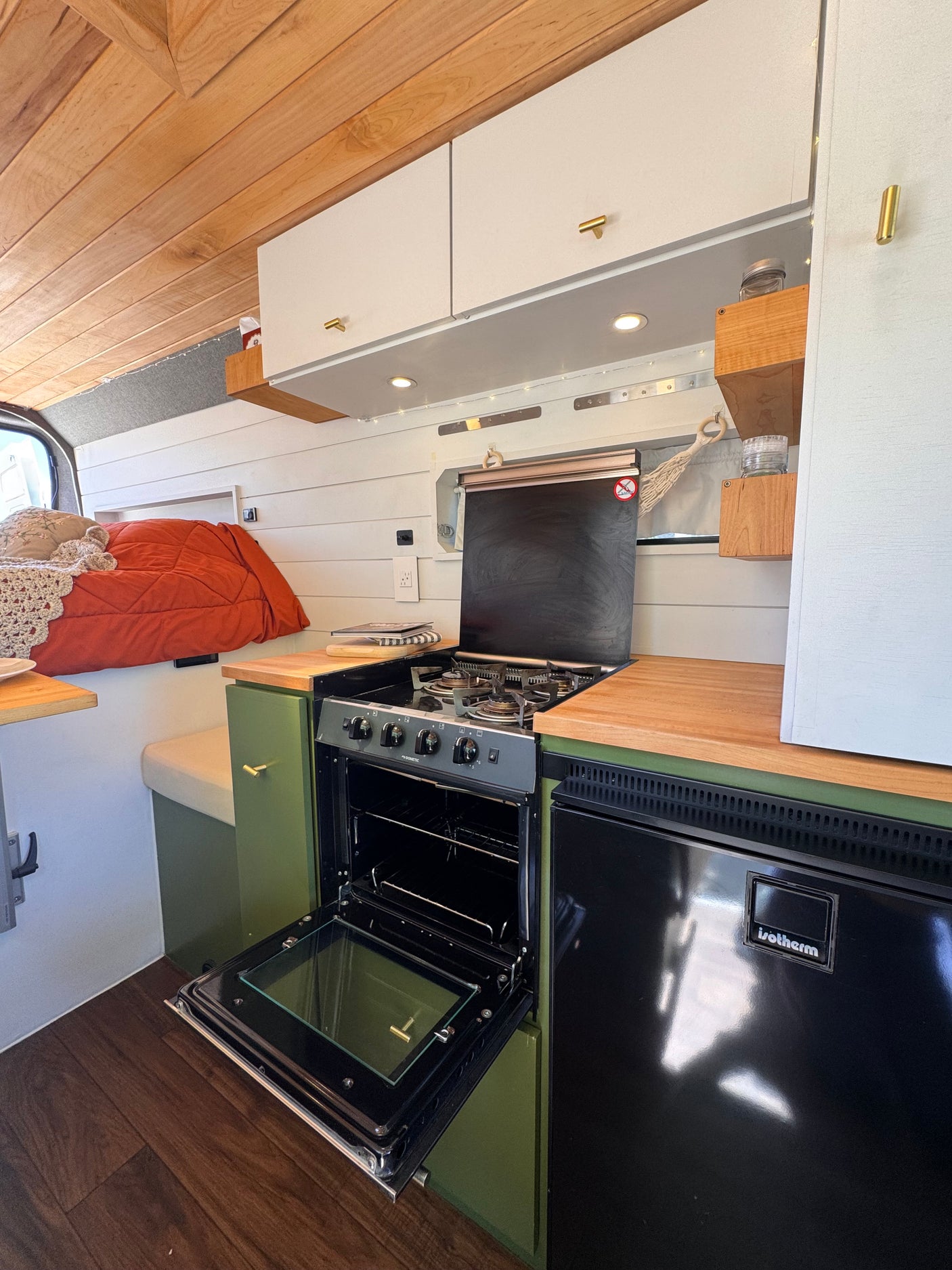 An RV rental's cozy kitchen area, showing an open oven, a refrigerator, green cabinets, and warm wood accents.