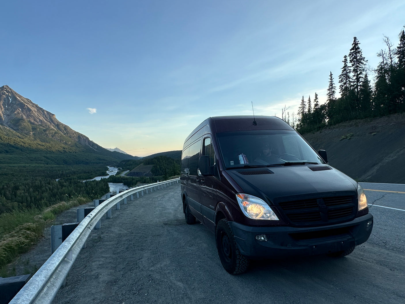 Experience nature with an rv rental! A dark camper van is parked on a mountain pass overlooking a scenic valley with a river and forests.