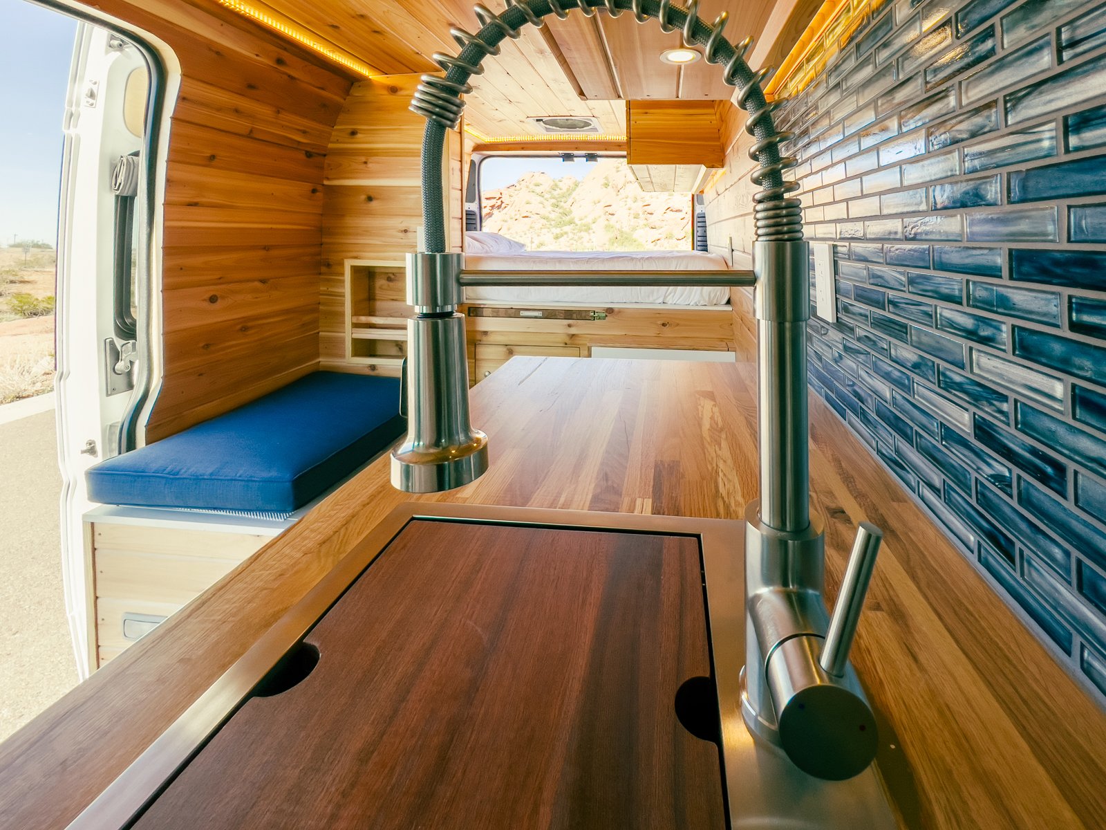 parked on a desert road with rocky hills.|Bright custom wood RV rental interior: bunk bed