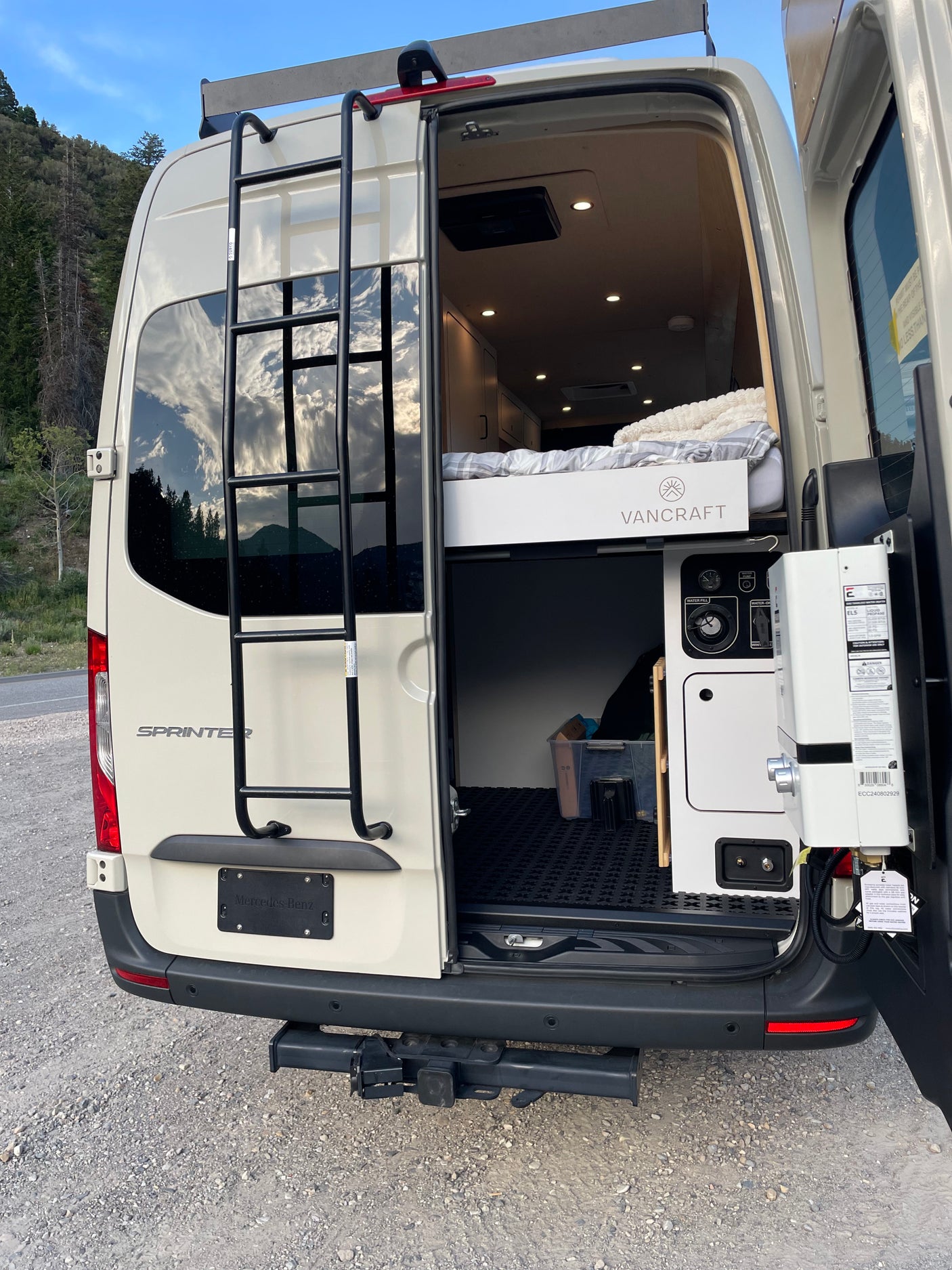 RV rental Sprinter camper van's rear view, with open doors showcasing its VANCRAFT interior, cozy bed, and water system.