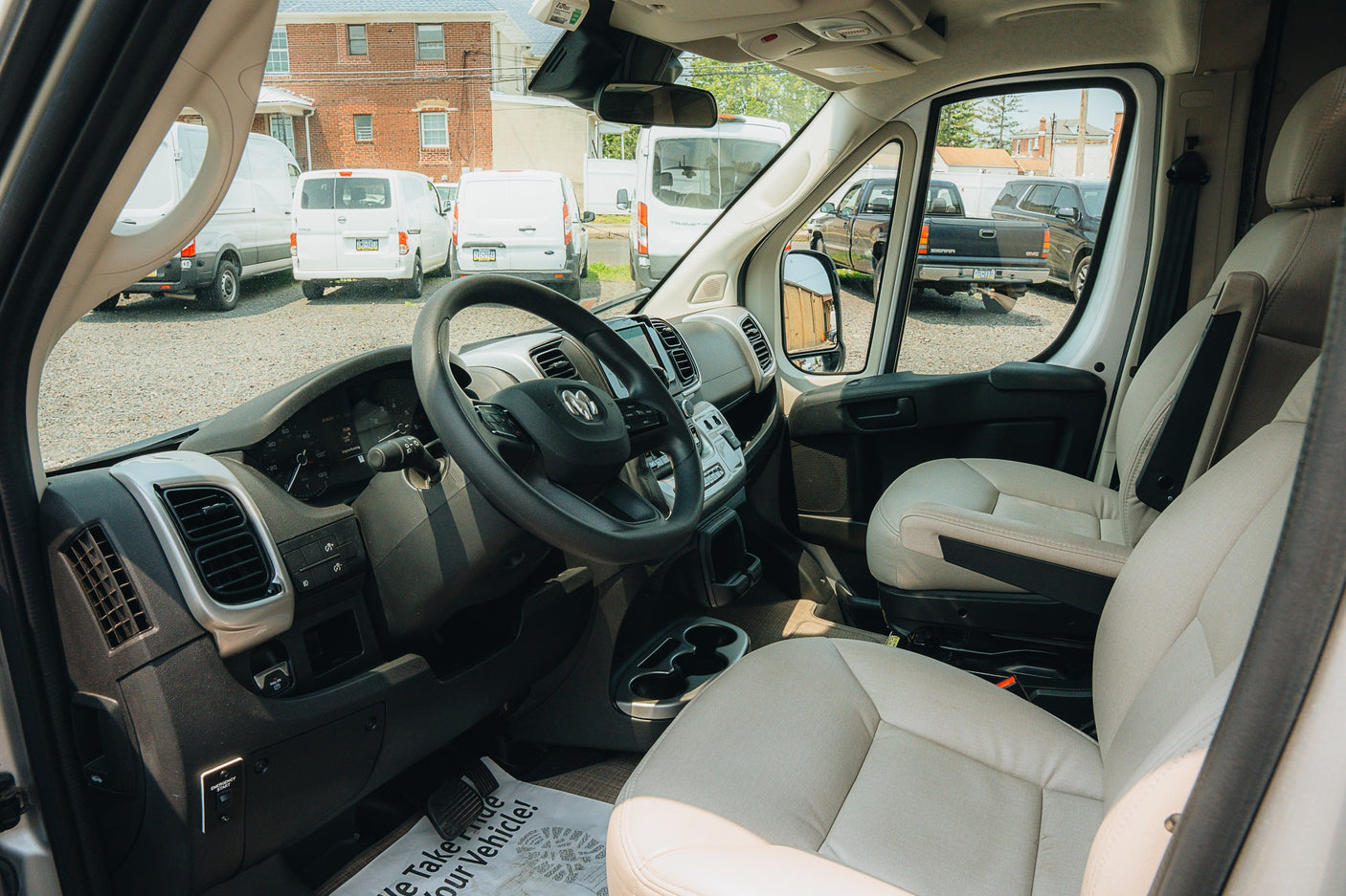 View of an RV rental van's interior: driver's seat, dashboard, and steering wheel. Other vans are visible outside.