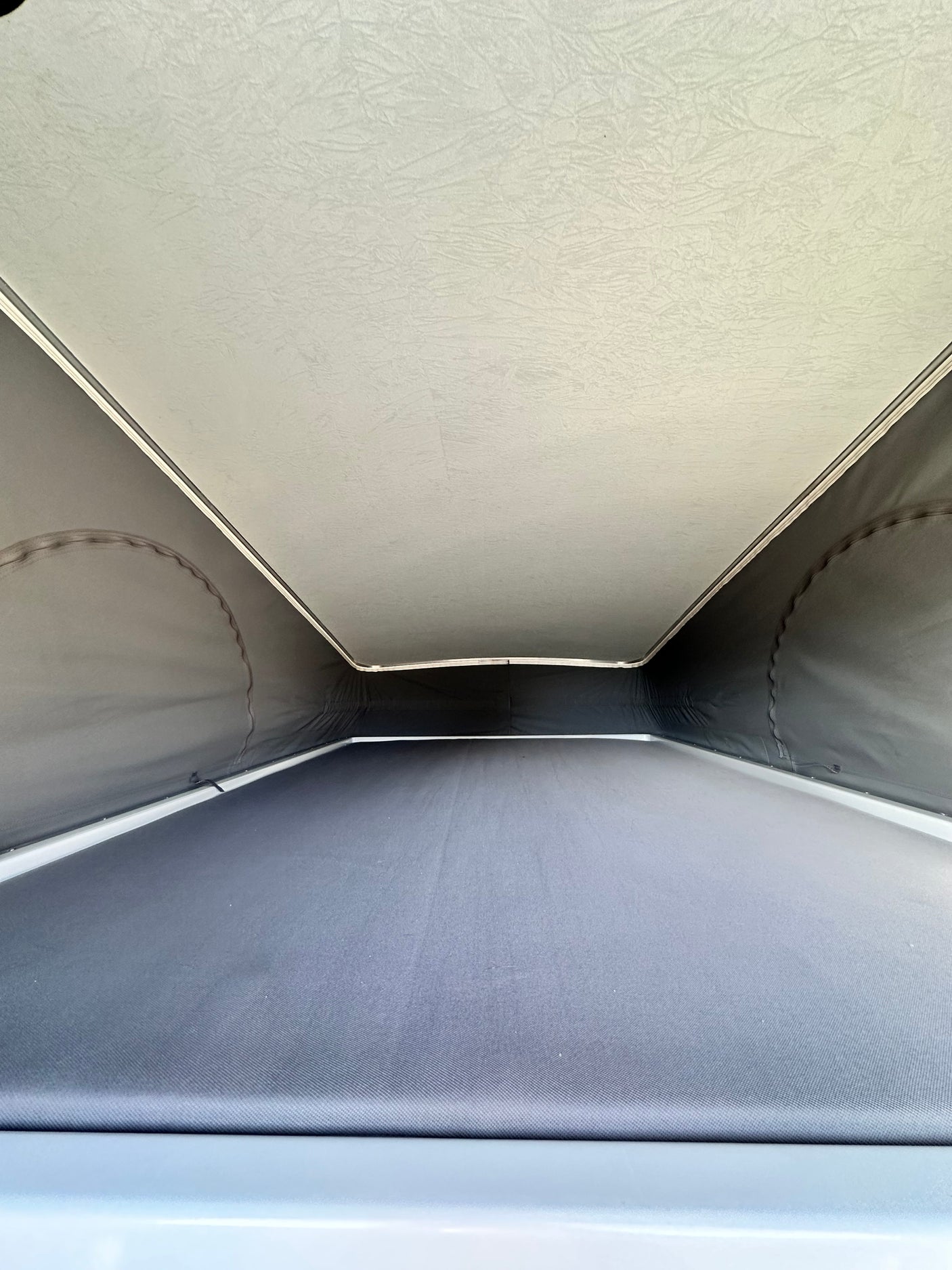 RV rental pop-top camper's interior: View of the light-colored elevated sleeping area and dark fabric walls.