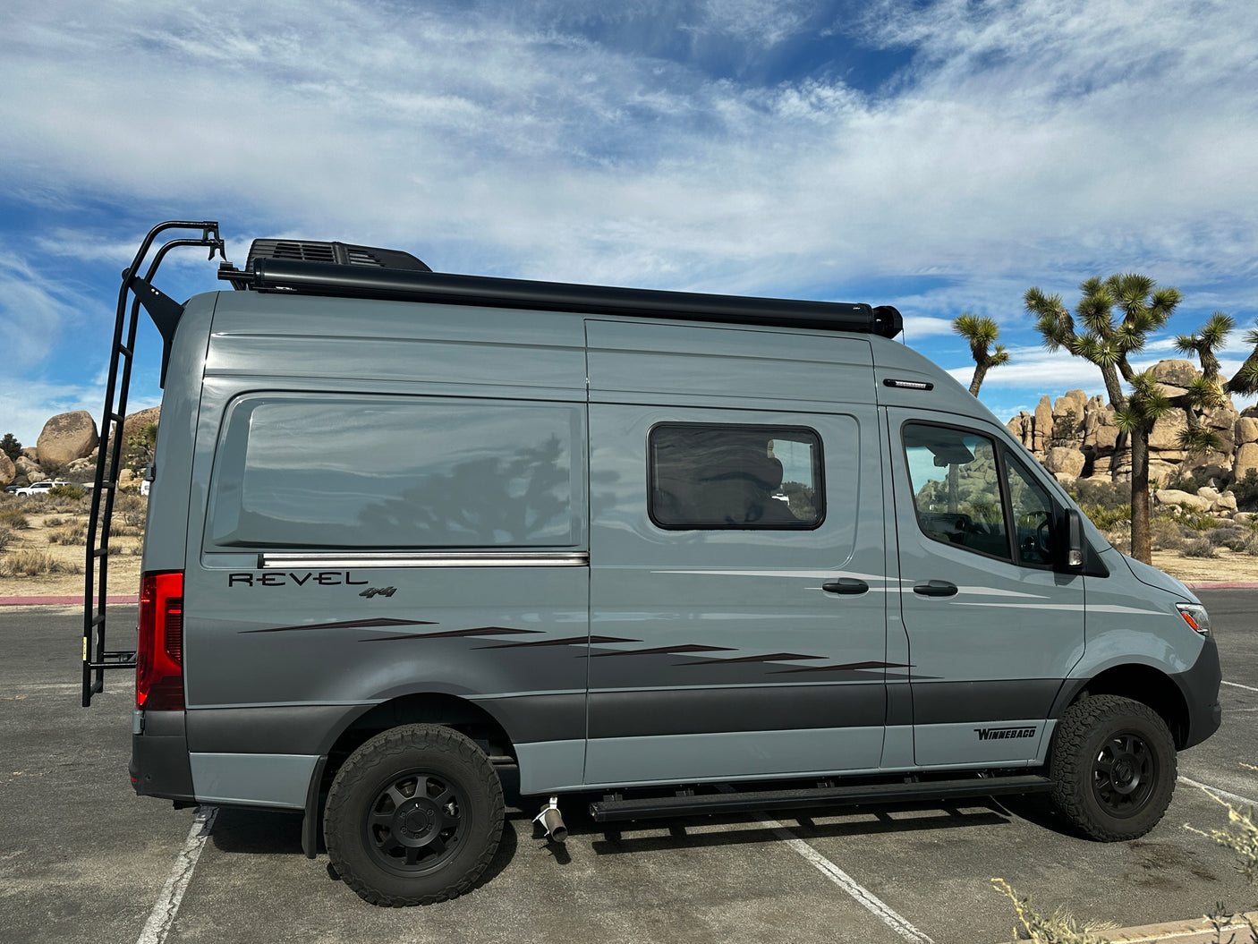 Sleek gray Winnebago Revel 4x4 camper van, ideal for rv rental adventures, parked among Joshua Trees.