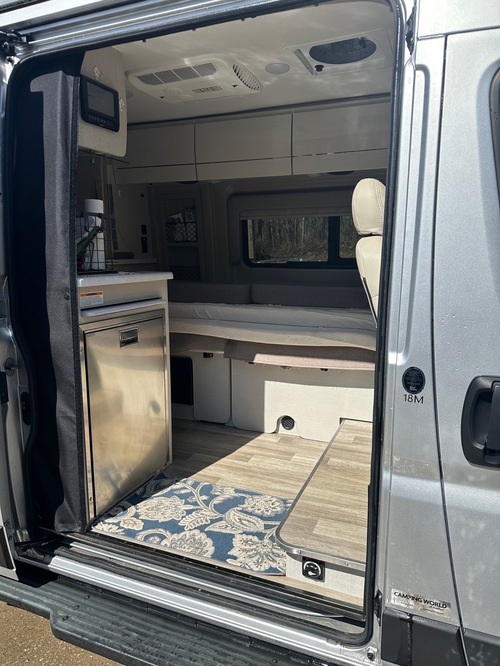 View into a sleek RV rental, revealing a compact kitchen with a stainless steel fridge, bed, and pop-up table inside.