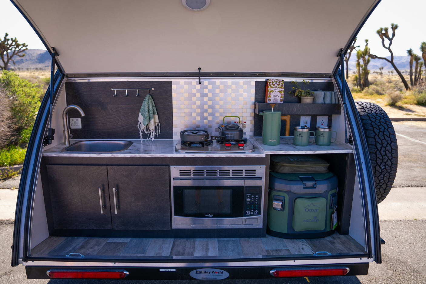 This RV rental teardrop camper reveals its compact outdoor kitchen with sink, stove, microwave, and cooler, perfect for desert camping.