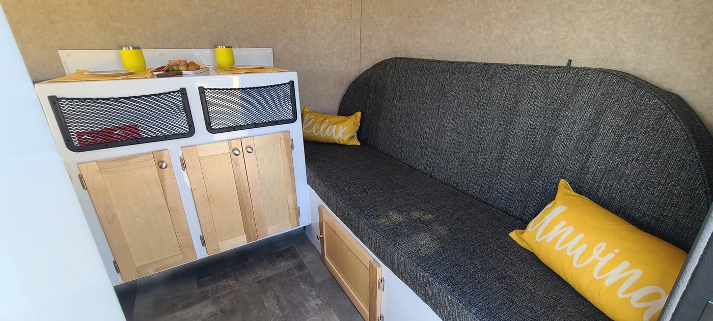 This rv rental features a cozy grey sofa with yellow pillows, a compact kitchenette with snacks, and storage cabinets. — photo 14