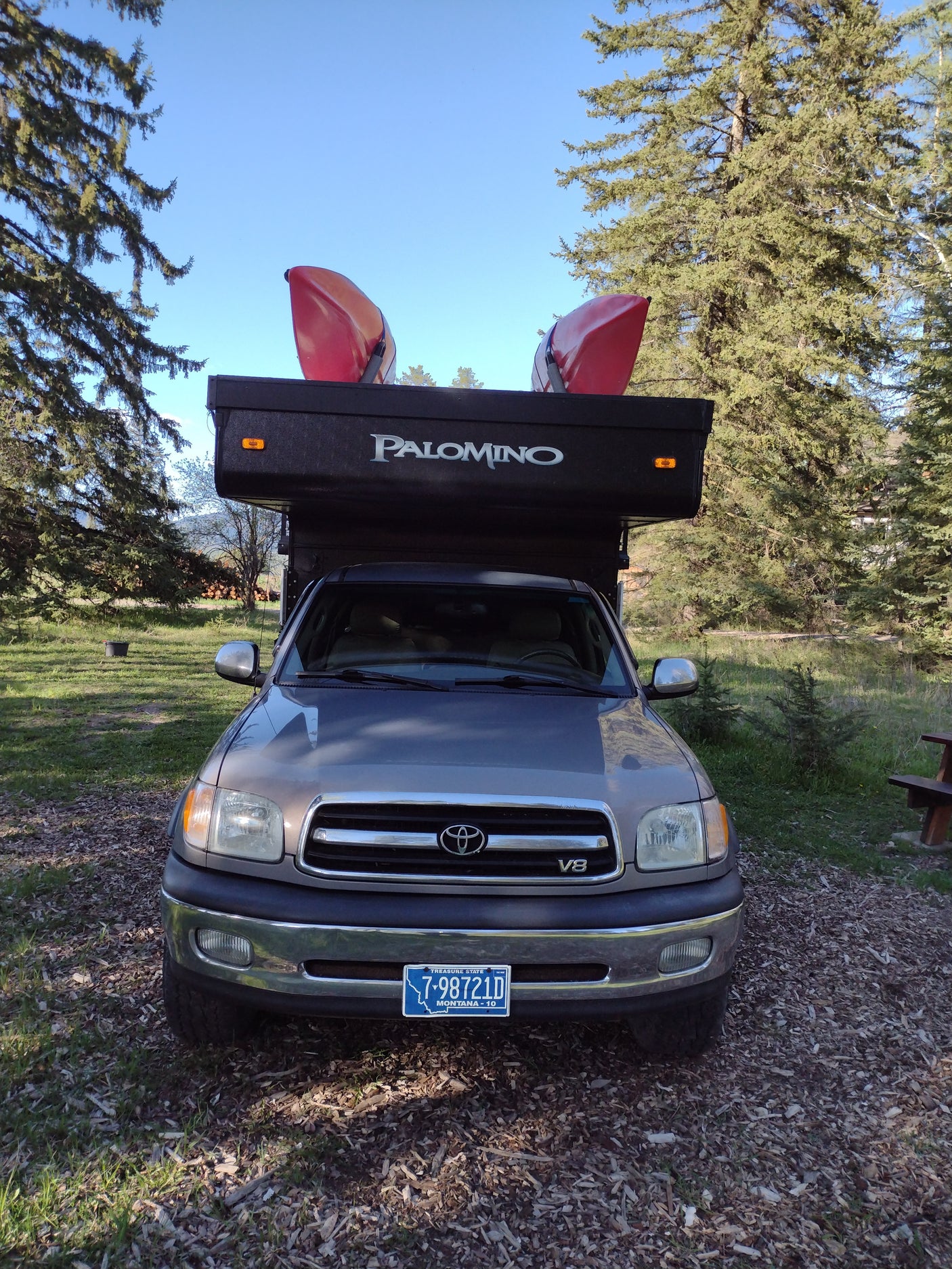 An RV rental: a grey Toyota Tundra truck with a black Palomino pop-up camper, topped with two red kayaks, ready for outdoor adventure.