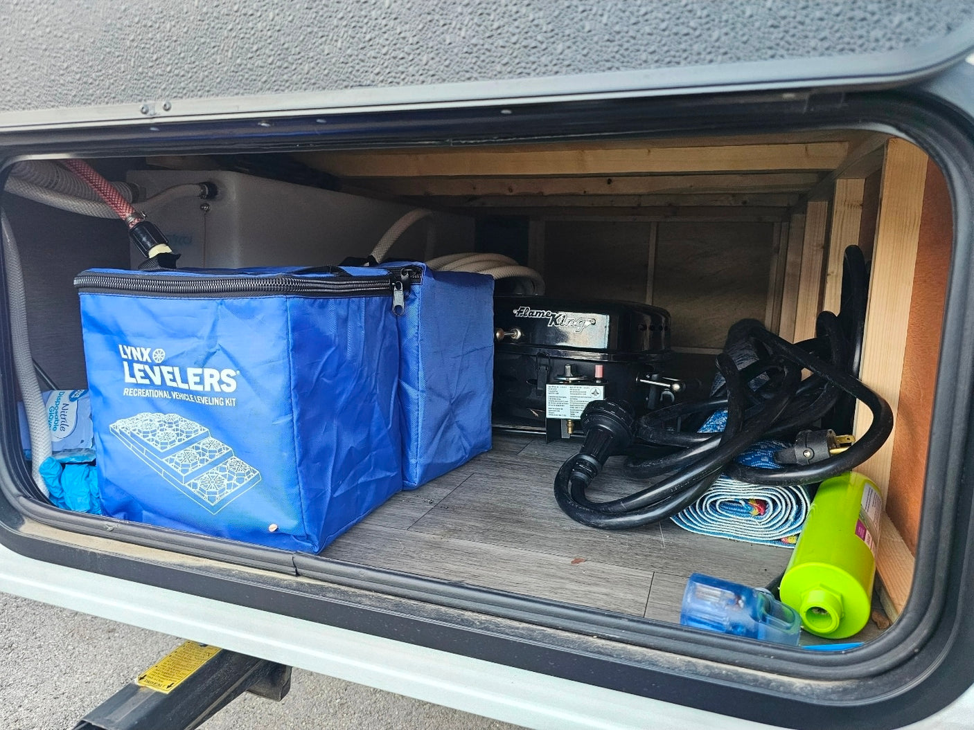 RV rental under-storage: Lynx Levelers, Flame King grill, power cord, & essentials for camping trips.