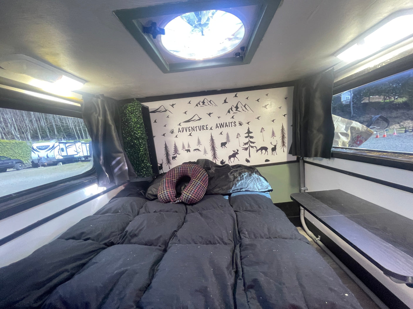 Relax in this cozy rv rental bed with an 'Adventure Awaits' wall. Perfect for travel exploration and comfortable stays.