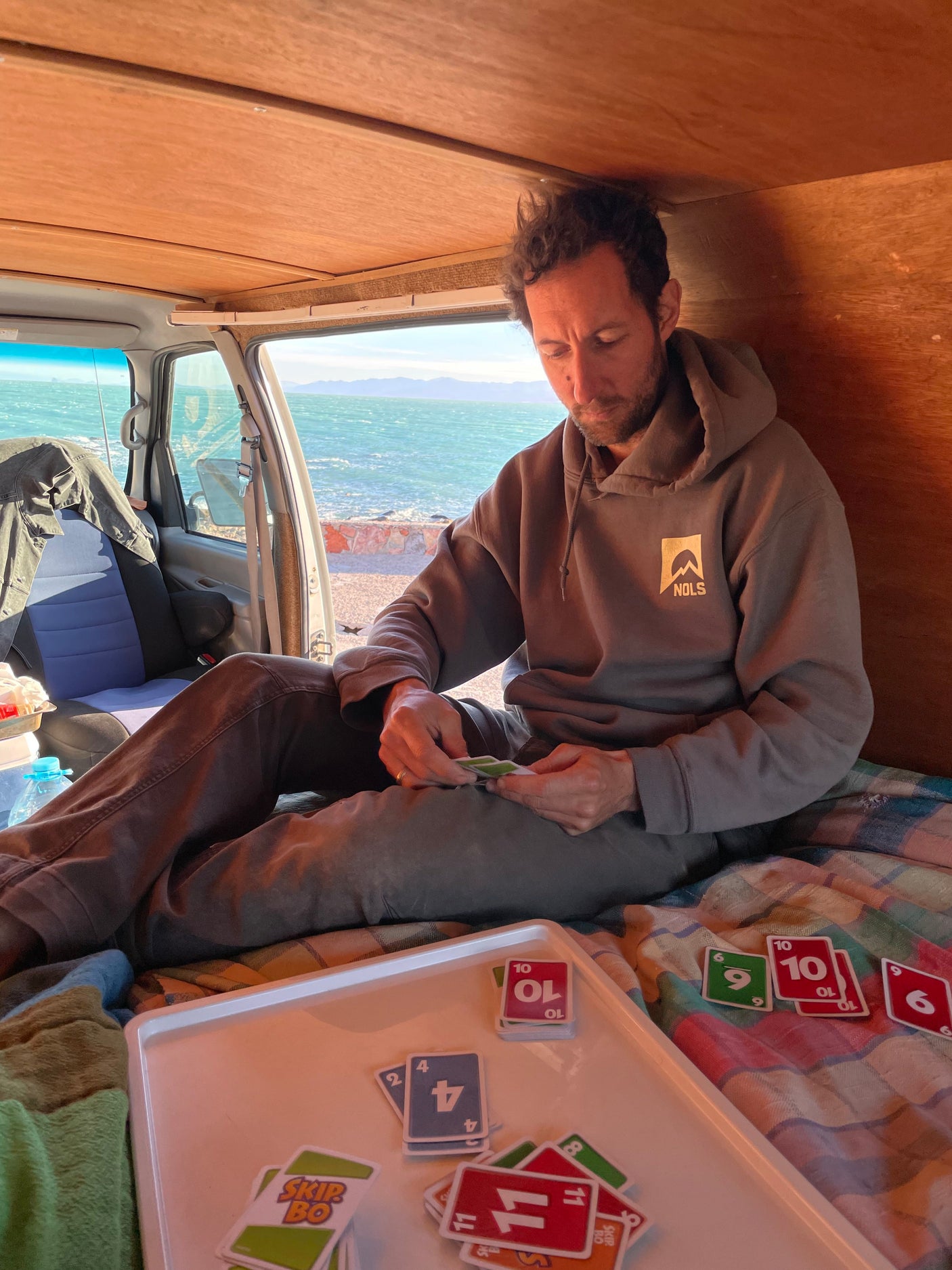 Man plays Skip-Bo in an rv rental van, enjoying ocean views. Ideal for a relaxed road trip.