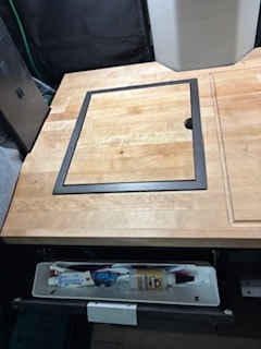 Inside an **rv rental**: wooden kitchen counter with a flush lid over a sink, and pull-out toiletry storage below.