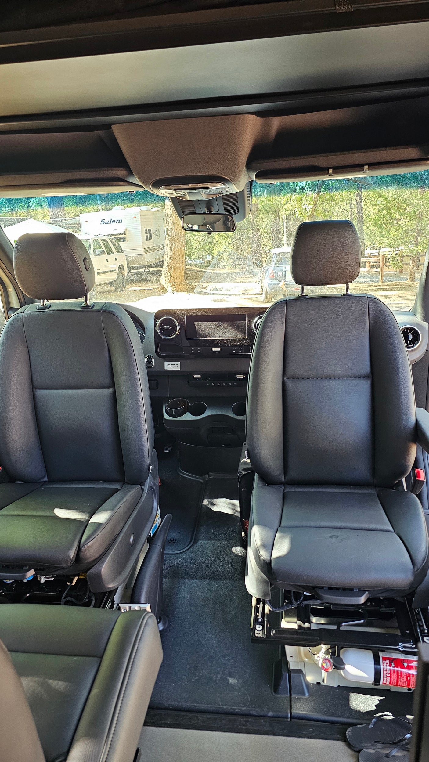 Inside an RV rental: front seats, dashboard, and a view of the campground through the windshield.