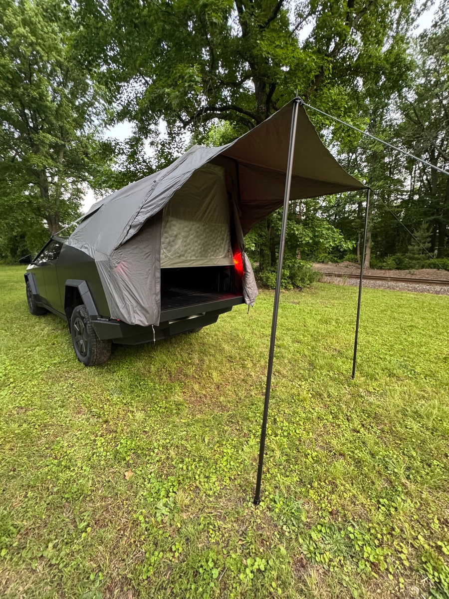 Innovative Cybertruck camping setup, potentially for an RV rental, with a rear tent and awning in a grassy field.