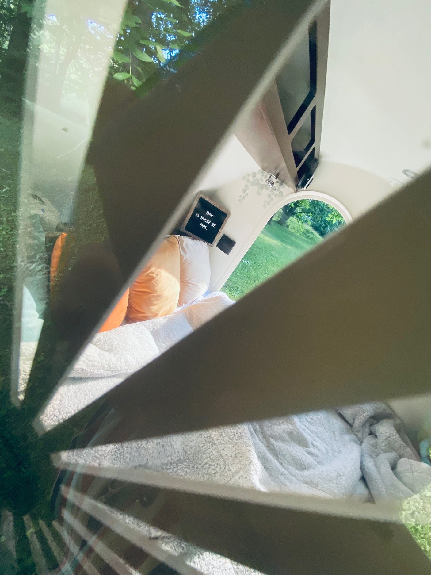 Experience a cozy RV rental: complete with bed, pillows, and an arched window looking out to nature. "Home is where we park."
