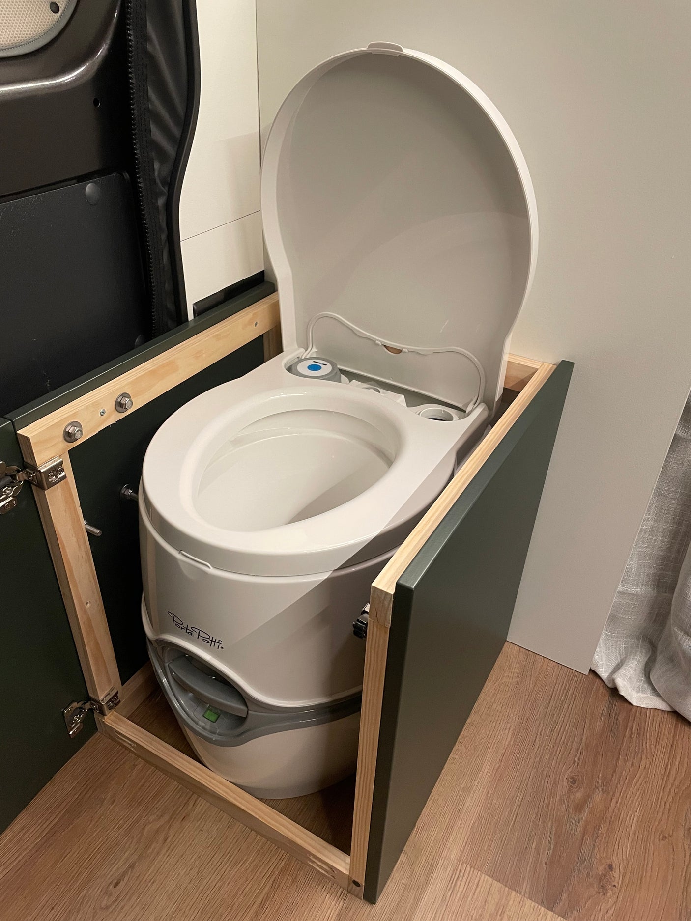 White portable toilet, lid open, integrated into a custom cabinet within an RV rental. Essential for comfortable van life.