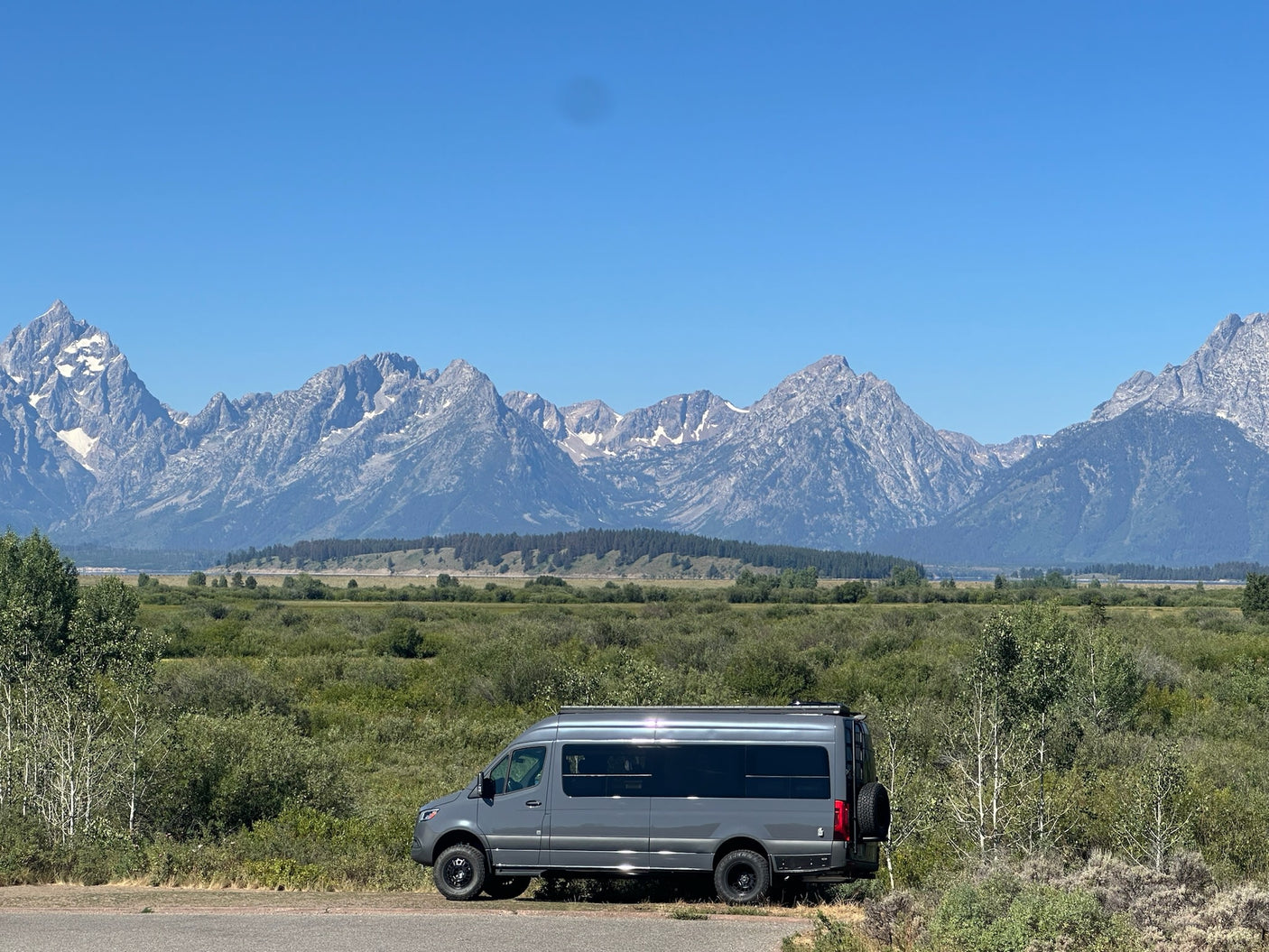 with stunning mountains & green landscape under a clear blue sky. Ideal for road trips.|This sleek grey custom Sprinter van