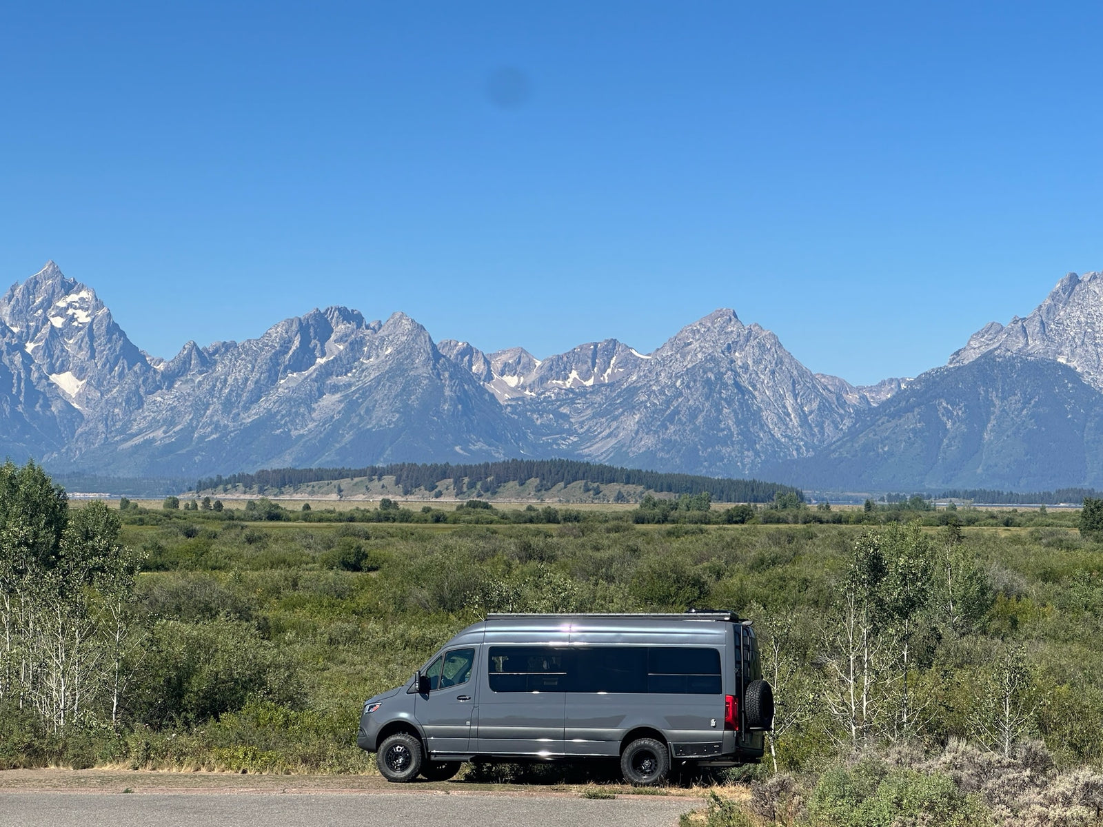 with stunning mountains & green landscape under a clear blue sky. Ideal for road trips.|This sleek grey custom Sprinter van