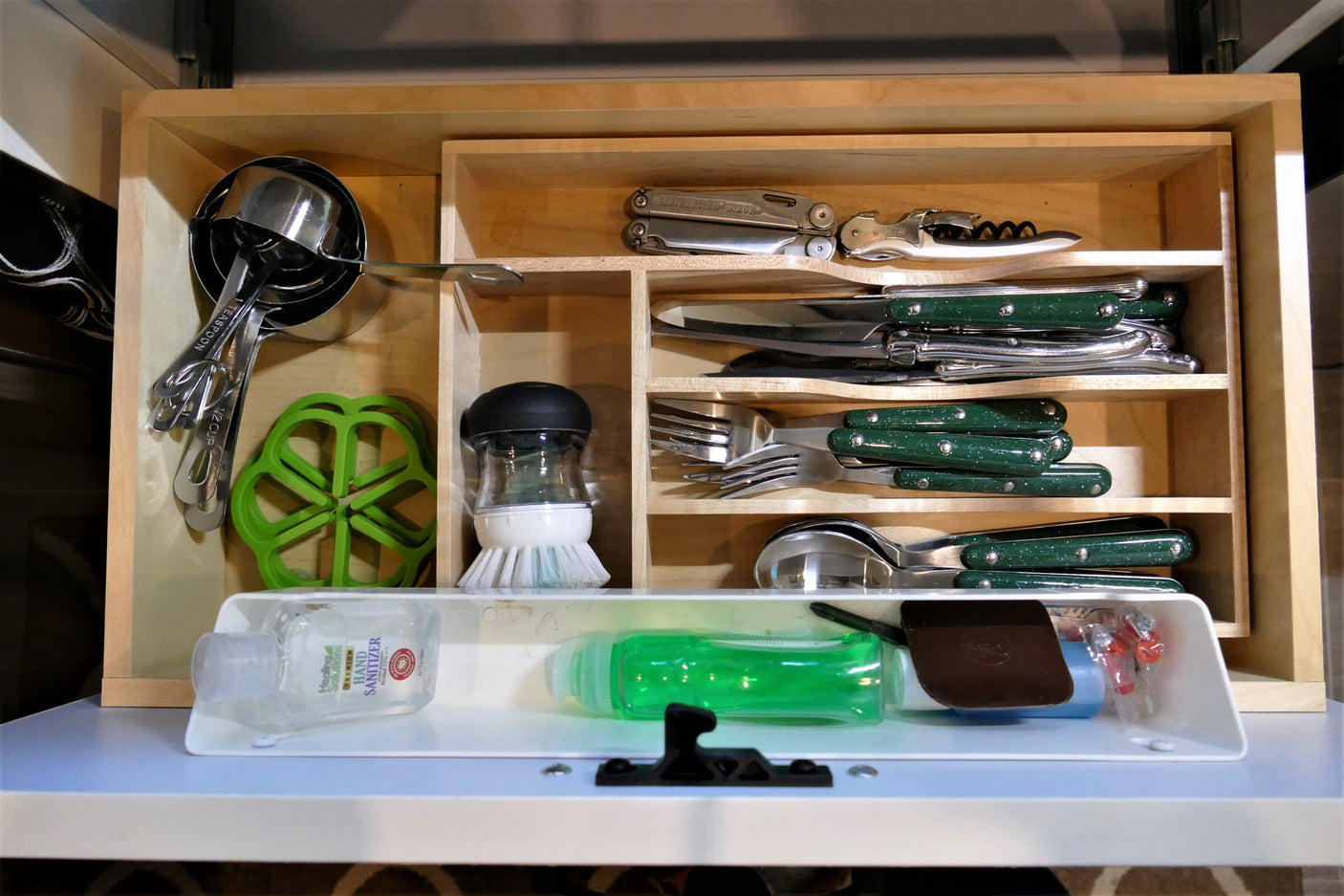 Organized kitchen & camping essentials for your RV rental: cutlery, measuring tools, multi-tool, and cleaning supplies neatly stored.