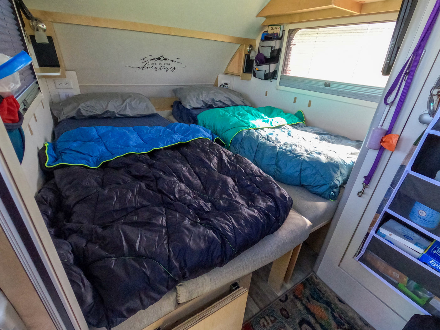 Cozy rv rental interior with two beds, sleeping bags, an adventure wall decal, and pet-friendly amenities like a leash.