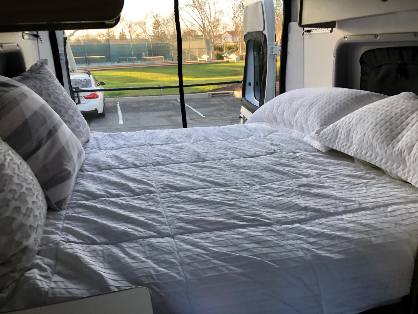 Inside an RV rental: Relax on this cozy bed with an open view of a park and tennis courts outside.