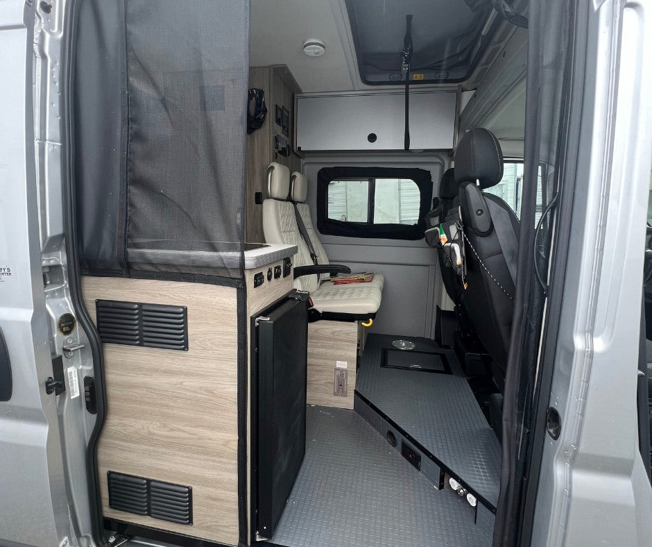 RV rental interior: View of compact kitchen, fridge, and swiveling seats inside a modern camper van.