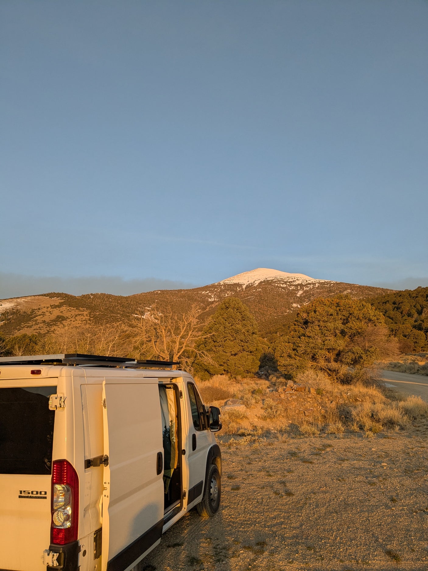 White camper van (RV rental) parked at golden hour, revealing its interior, with snow-capped mountains in the background.